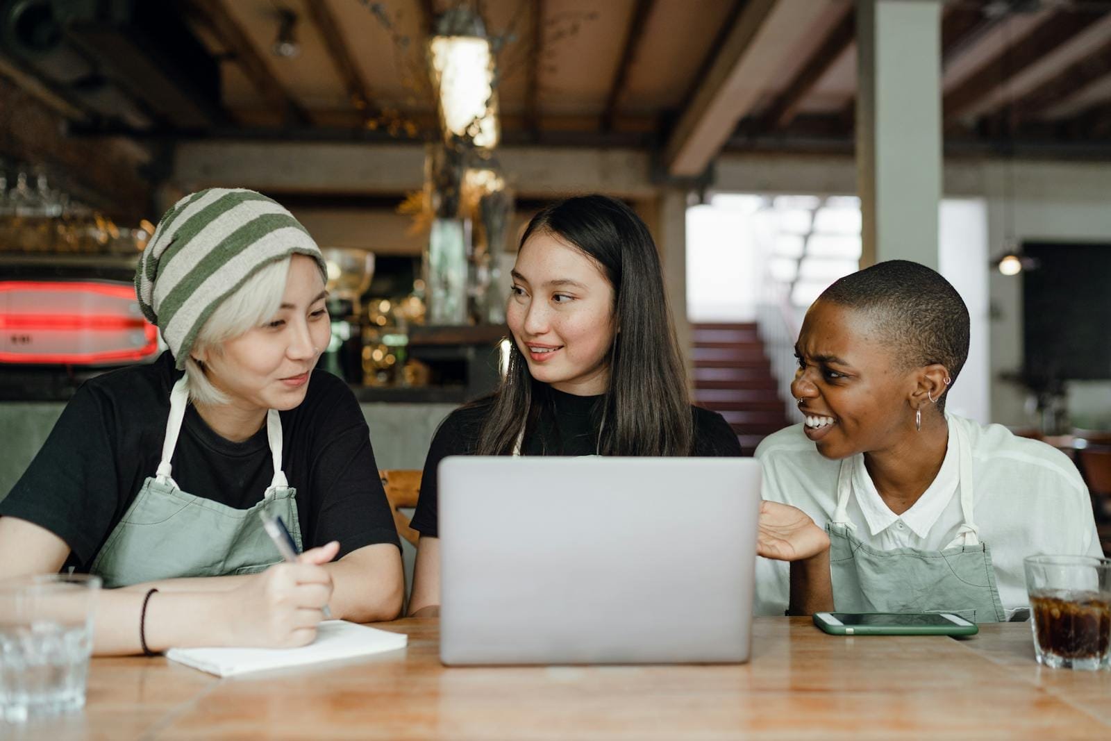 Three cafe team members laughing and working on a laptop, showcasing Happy Pixel Designs' ability to connect with small businesses for impactful web designs.