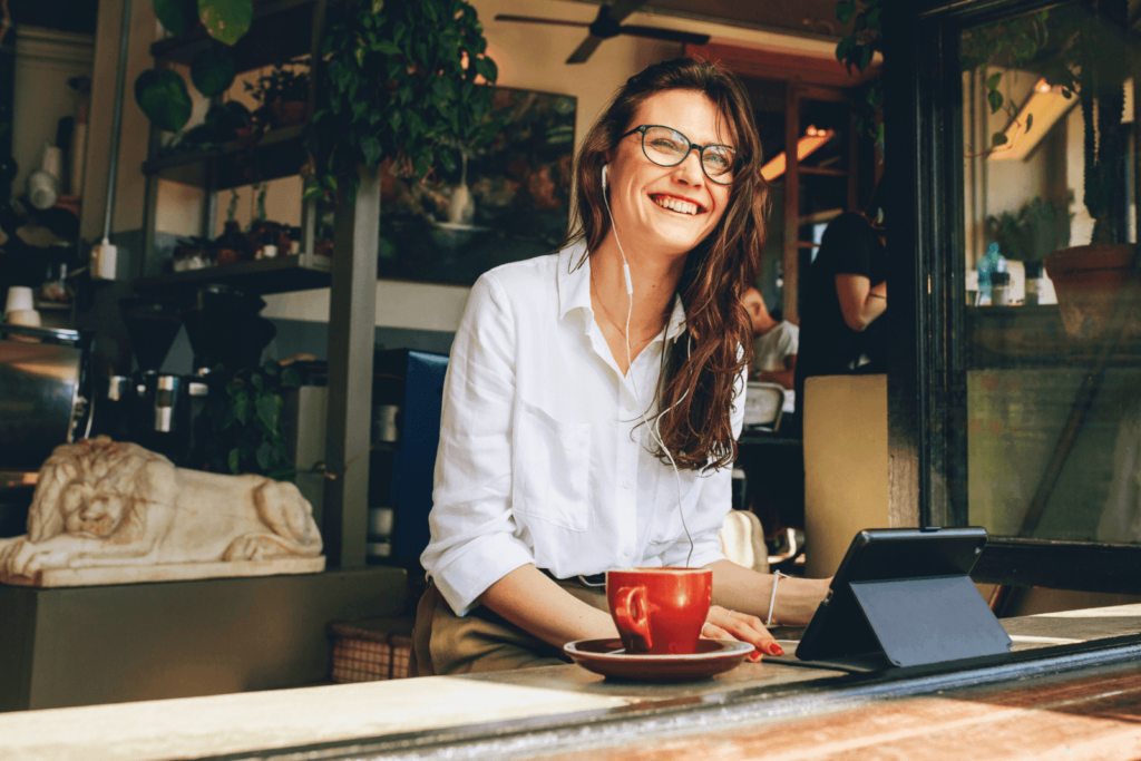 A smiling entrepreneur works on a tablet with a coffee cup on the table in a cozy café setting.