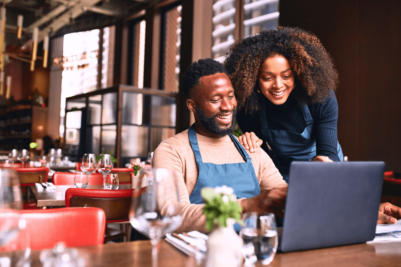 Two restaurant owners smiling and collaborating on a laptop in a cozy restaurant setting, reflecting Happy Pixel Designs' supportive approach to helping small businesses succeed online.