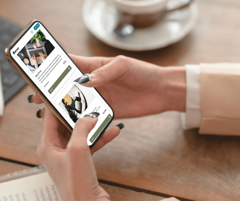 A person with stylish nails browses a shopping app on their smartphone, sitting at a wooden table with a coffee cup.