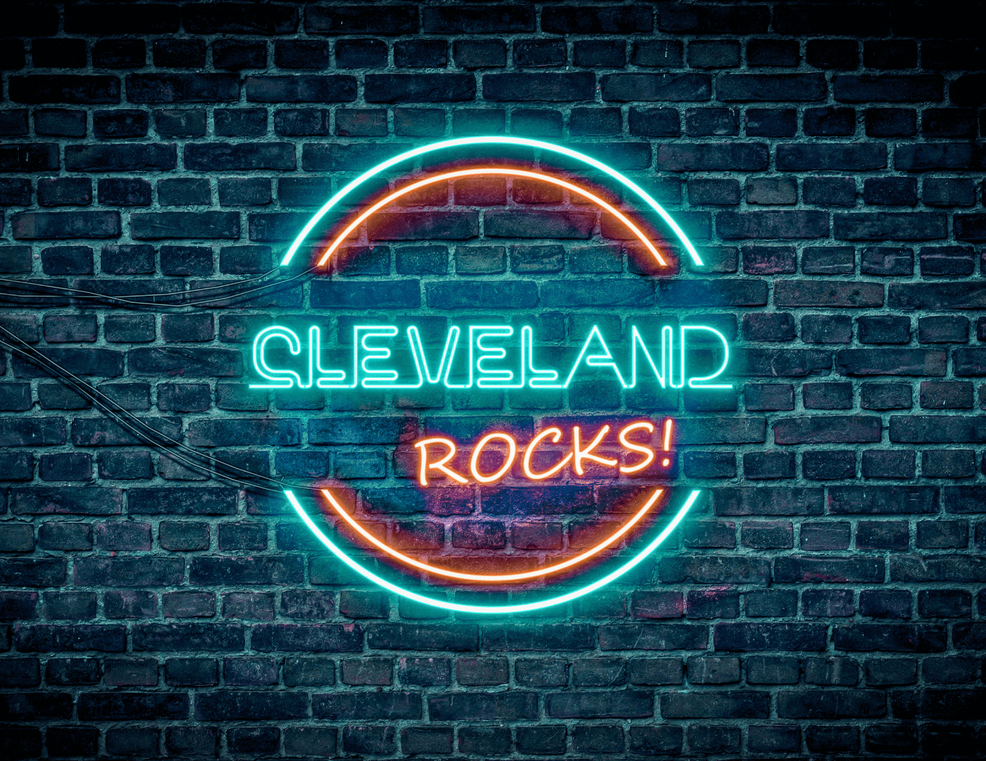Neon sign reading "CLEVELAND ROCKS!" in vibrant blue and orange on a dark brick wall background.