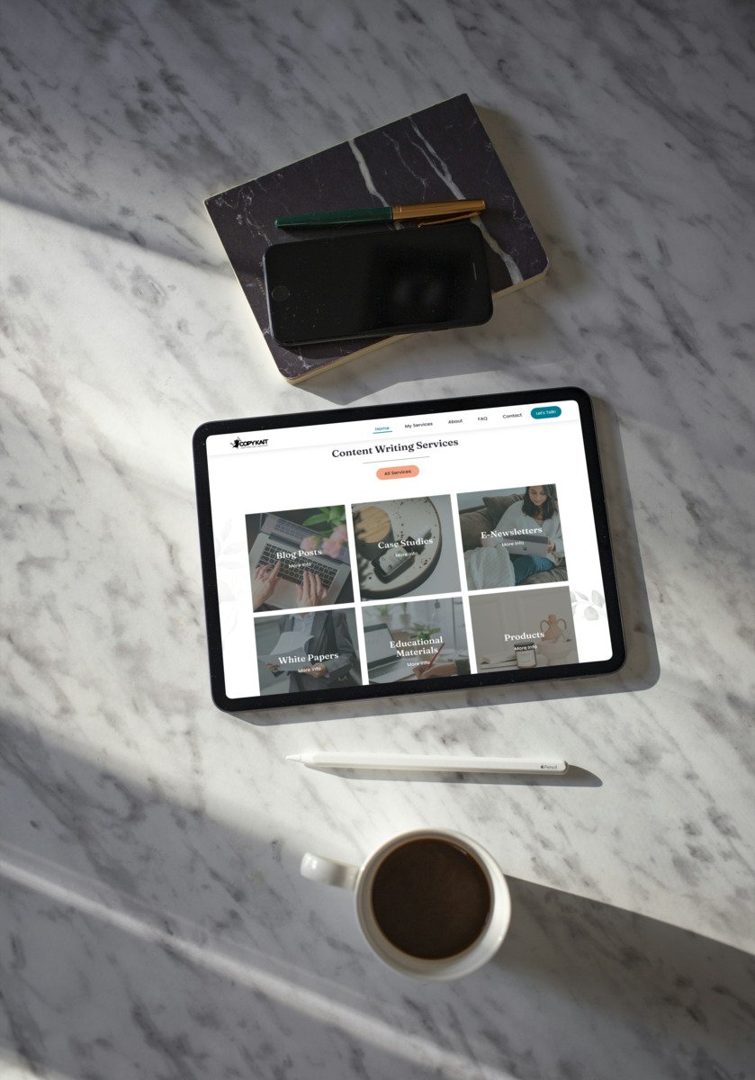 An overhead view of a tablet displaying custom writing services, a notebook, a phone, a pen, and a coffee cup on a marble table.