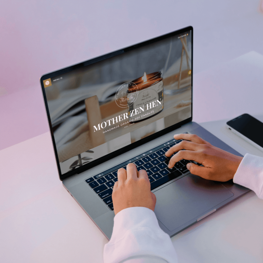 A person typing on a laptop displaying the "Mother Zen Hen" website, featuring handmade organic soy candles. Soft pastel background.